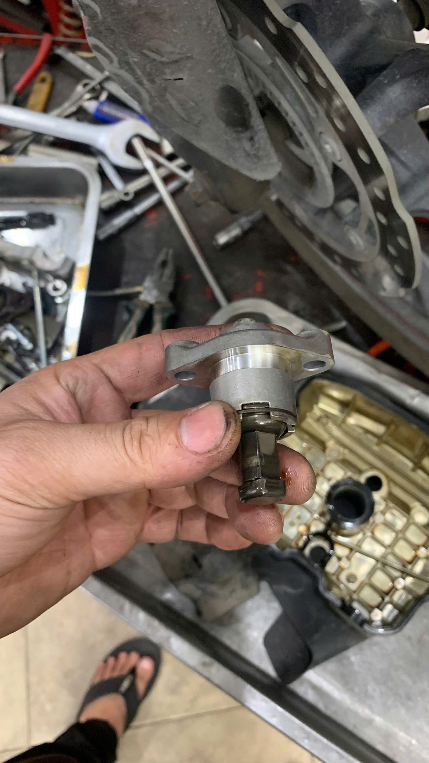 A mechanic holding a faulty Honda Winner cam chain tensioner, a common cause of engine noise.