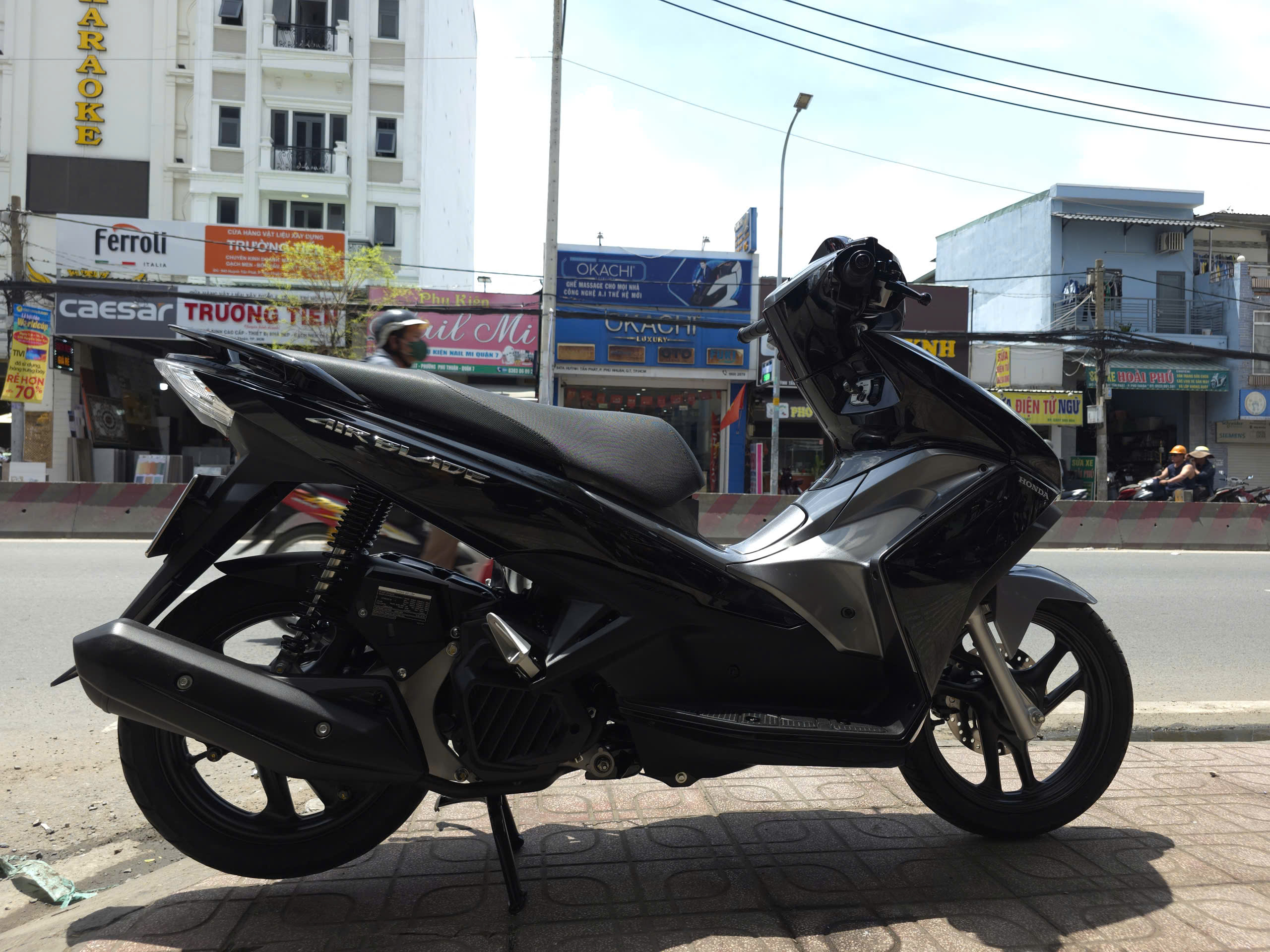 The restored black Honda Air Blade parked on a city street, looking brand new after scooter engine repair and bodywork.